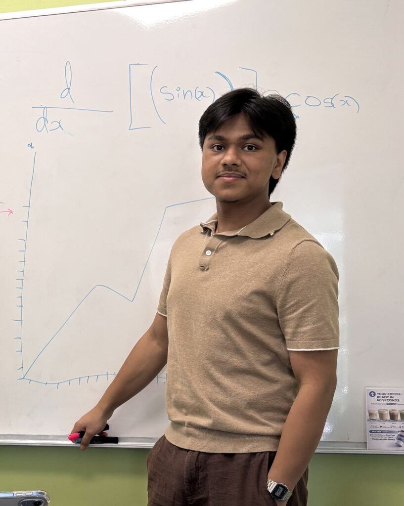 Rudra, Calgary Minds math and physics tutor, smiling in front of a whiteboard